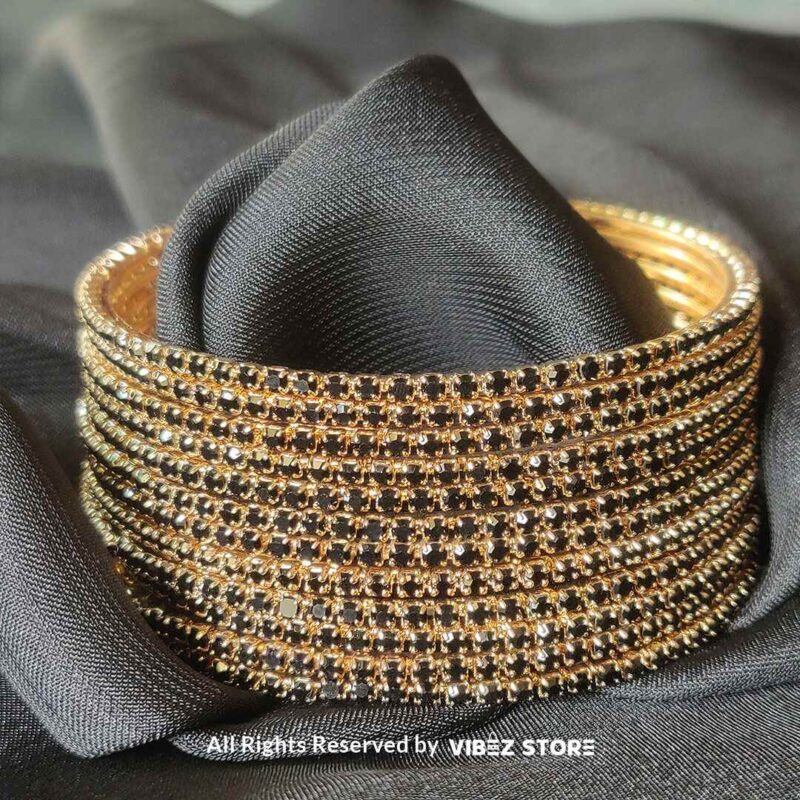 Multi-layer gold bangle set with black crystal accents on a black fabric background