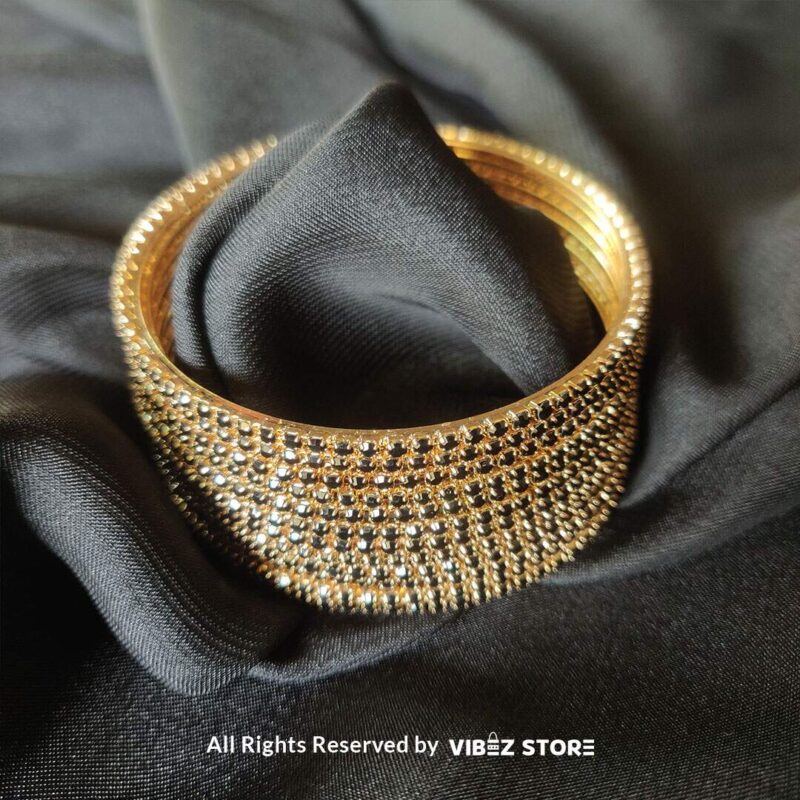 Multi-layer gold bangle set with black crystal accents on a black fabric background