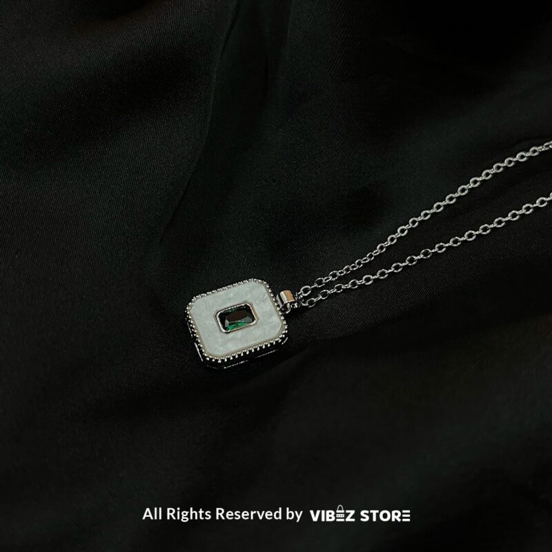 Square Gemstone & Mother-of-Pearl Locket with green gemstone and silver-tone chain on a black background