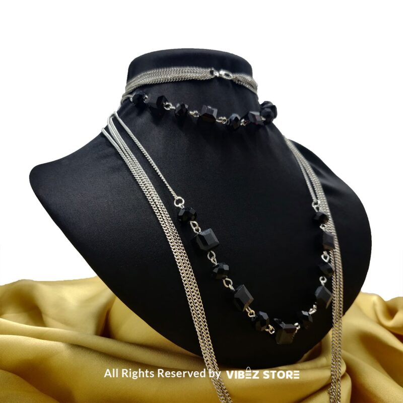 Elegant crystal cube and silver-tone chain necklace set on a black bust with yellow fabric background