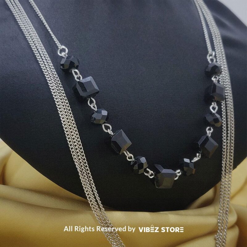 Elegant crystal cube and silver-tone chain necklace set on a black bust with yellow fabric background