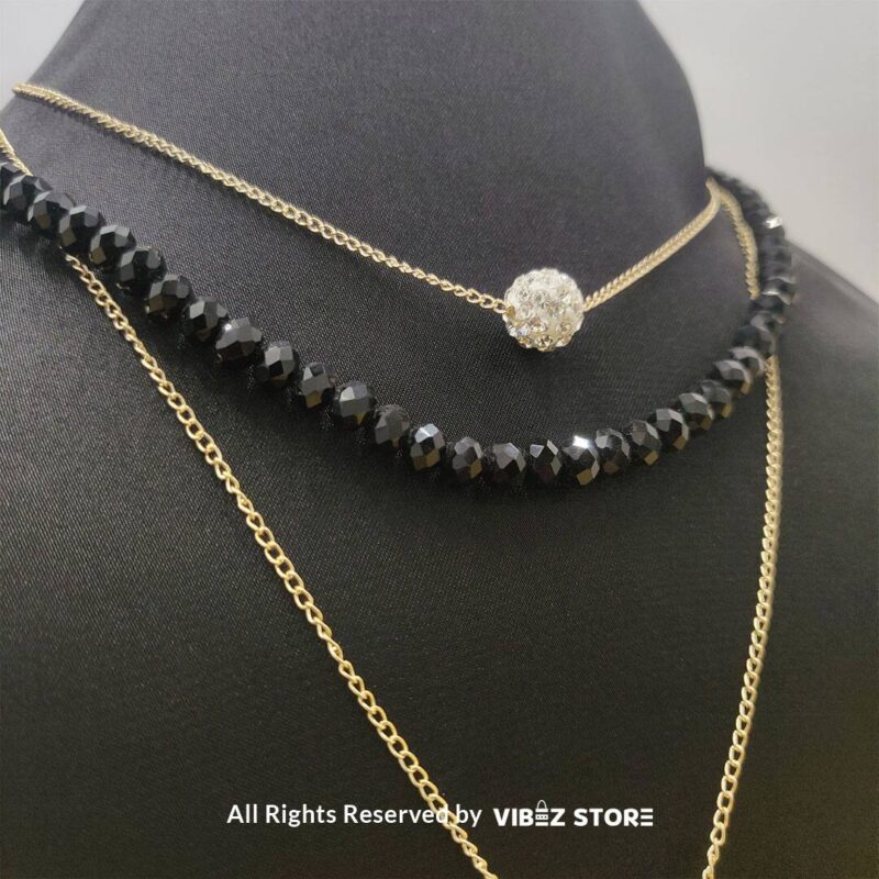 Triple-layer necklace with black beads, gold chains, and crystal ball accent displayed on black bust