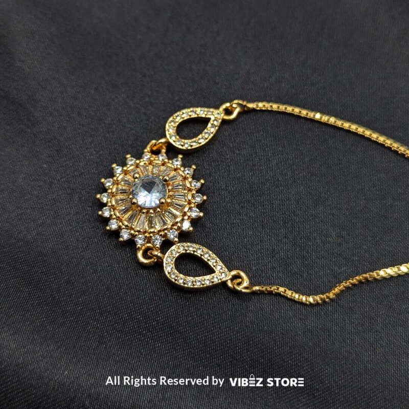 Gold-tone adjustable bracelet with sunburst crystal centerpiece and teardrop accents on black fabric background