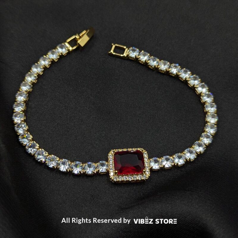 Two crystal-studded gold bracelets with square gemstone centerpieces in ruby red and soft pink on a black fabric background. 