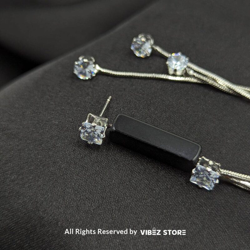 Stylish silver drape earrings with black accents and sparkling cubic zirconia details displayed on a black satin fabric.