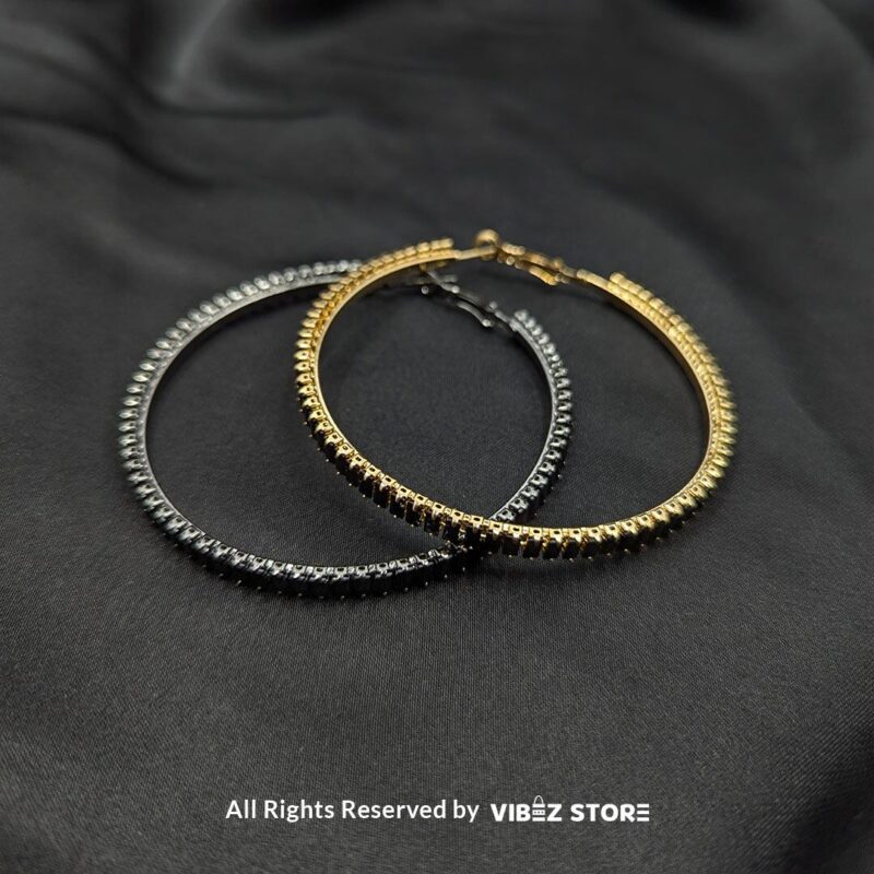 Crystal hoop earrings in gold and black displayed elegantly on a black fabric background.