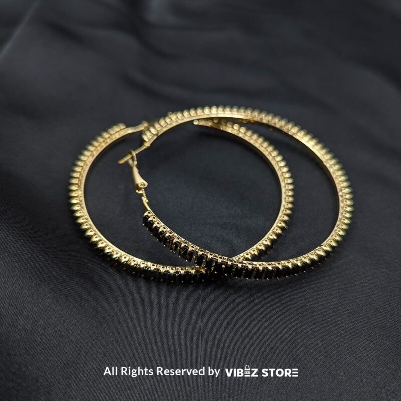 Crystal hoop earrings in gold and black displayed elegantly on a black fabric background.