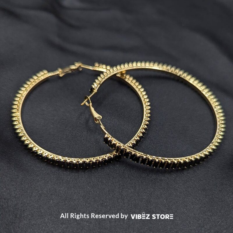 Crystal hoop earrings in gold and black displayed elegantly on a black fabric background.