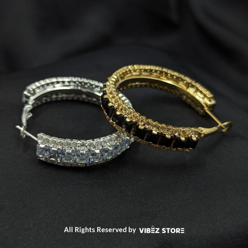 Gold hoop earrings with black crystals and silver hoop earrings with clear crystals displayed against a black fabric background.