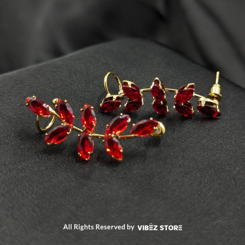 Golden earrings with vibrant marquise-cut red crystals arranged in a leaf pattern displayed on a black fabric background.