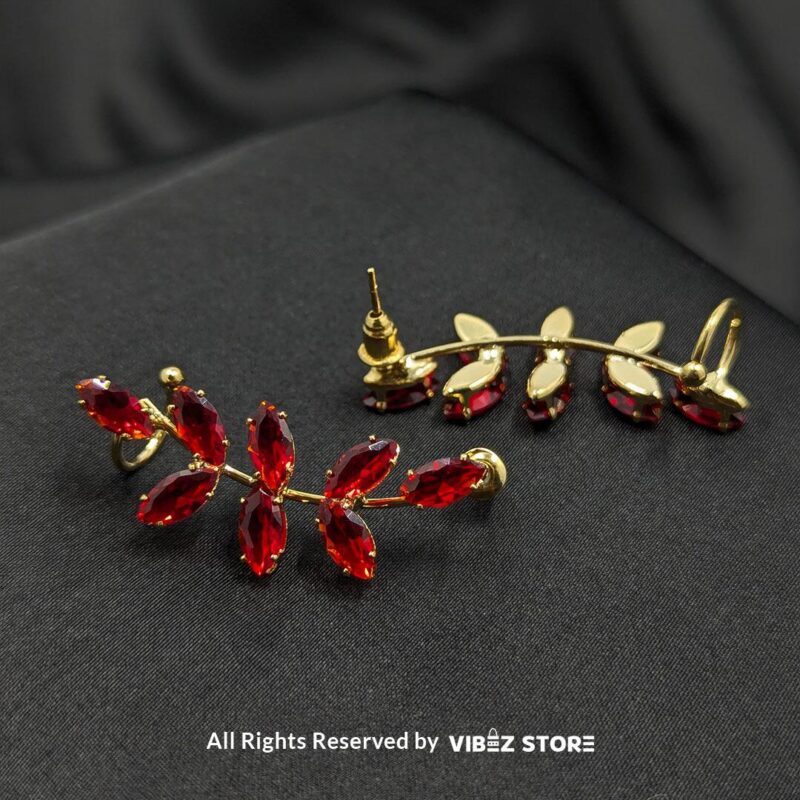 Golden earrings with vibrant marquise-cut red crystals arranged in a leaf pattern displayed on a black fabric background.