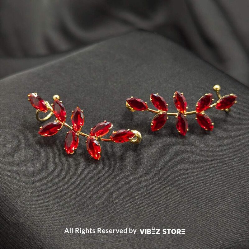 Golden earrings with vibrant marquise-cut red crystals arranged in a leaf pattern displayed on a black fabric background.