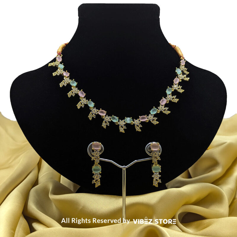 Gold-plated pastel gemstone necklace with matching drop earrings on a black display, featuring pink and green stones in floral motifs, ideal for weddings and festive occasions.