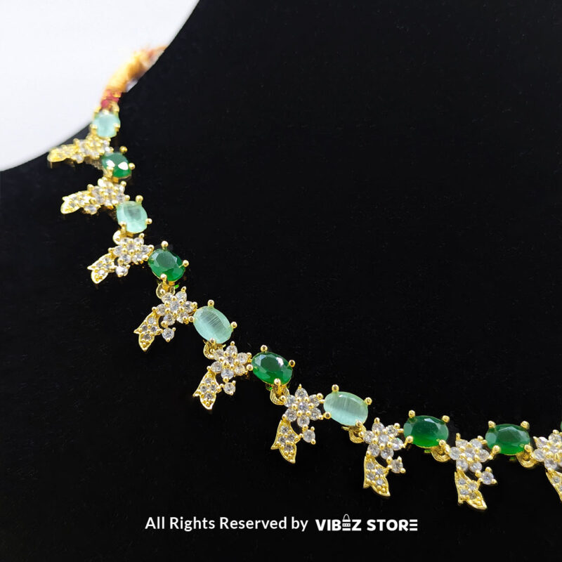 Gold-plated necklace set with vibrant green gemstones and a matching earring pair displayed on a black mannequin, perfect for weddings and formal events.