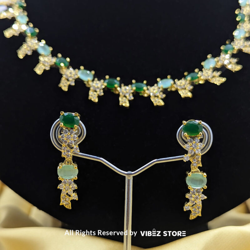 Gold-plated necklace set with vibrant green gemstones and a matching earring pair displayed on a black mannequin, perfect for weddings and formal events.