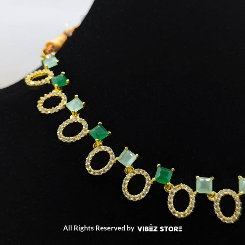 Gold-plated necklace set featuring oval and square green gemstones with matching drop earrings, elegantly displayed on a black mannequin.