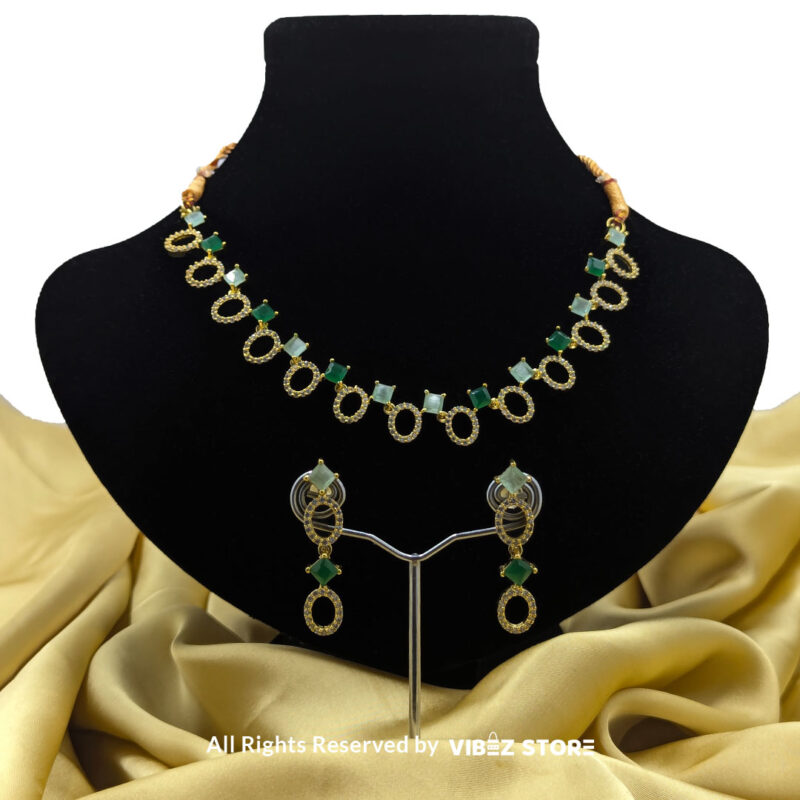 Gold-plated necklace set featuring oval and square green gemstones with matching drop earrings, elegantly displayed on a black mannequin.