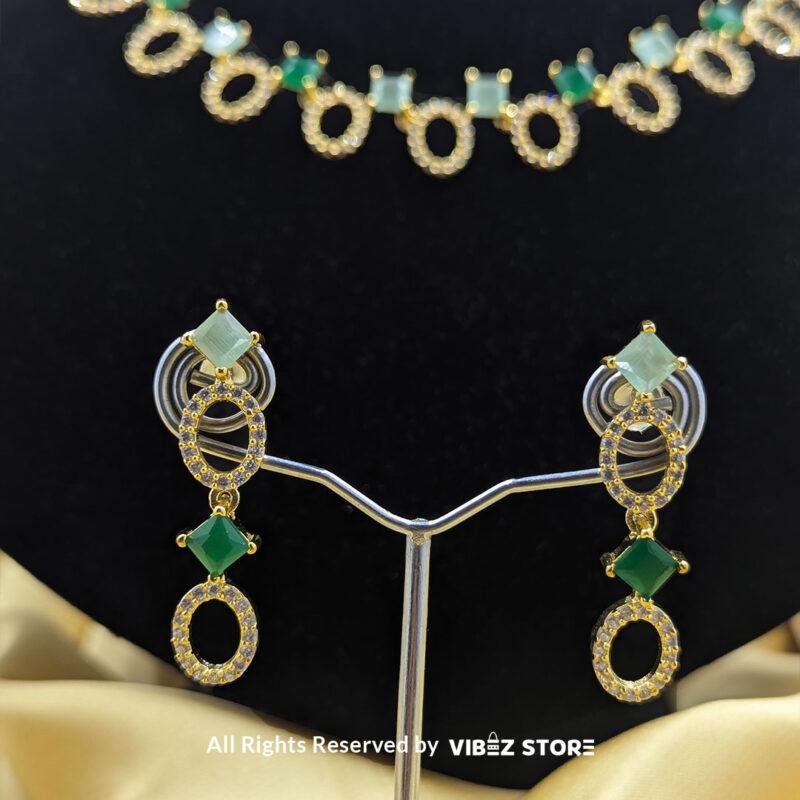 Gold-plated necklace set featuring oval and square green gemstones with matching drop earrings, elegantly displayed on a black mannequin.