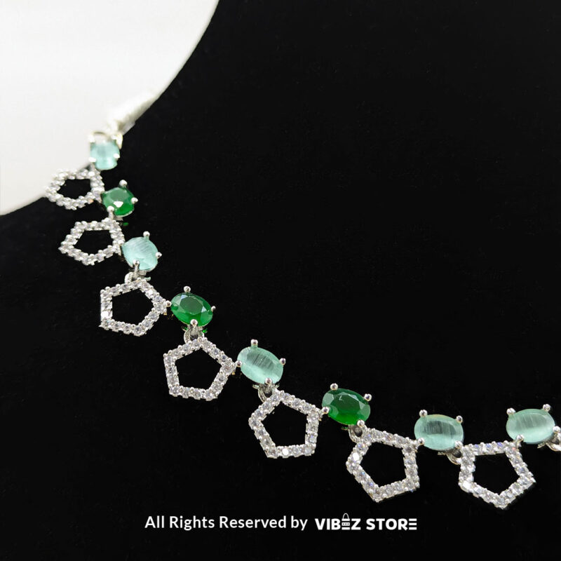 Silver-plated necklace with green gemstones in a geometric design, paired with matching drop earrings, displayed on a black mannequin.