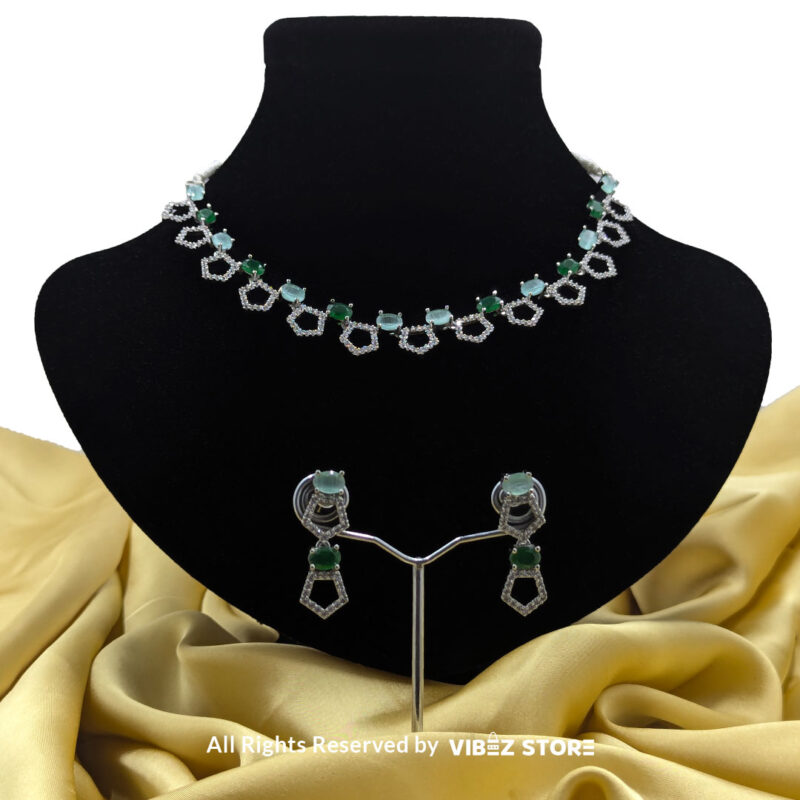 Silver-plated necklace with green gemstones in a geometric design, paired with matching drop earrings, displayed on a black mannequin.