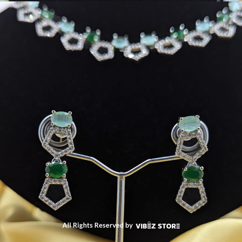 Silver-plated necklace with green gemstones in a geometric design, paired with matching drop earrings, displayed on a black mannequin.