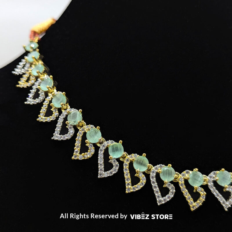 Dual-tone green gemstone necklace set with matching drop earrings, displayed on a black mannequin with a golden fabric backdrop.