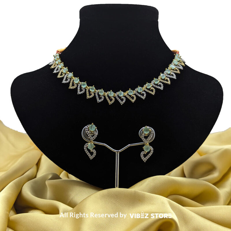 Dual-tone green gemstone necklace set with matching drop earrings, displayed on a black mannequin with a golden fabric backdrop.