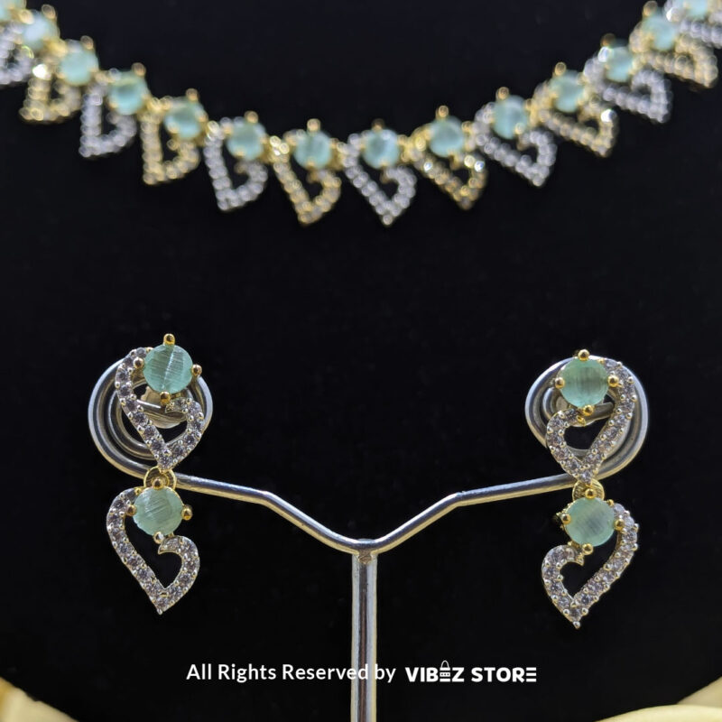 Dual-tone green gemstone necklace set with matching drop earrings, displayed on a black mannequin with a golden fabric backdrop.