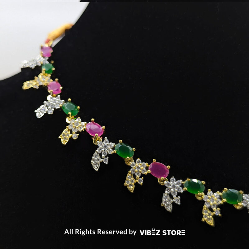 Multicolor gemstone necklace set with green and pink stones, paired with matching earrings, displayed on a black mannequin with a golden fabric backdrop.