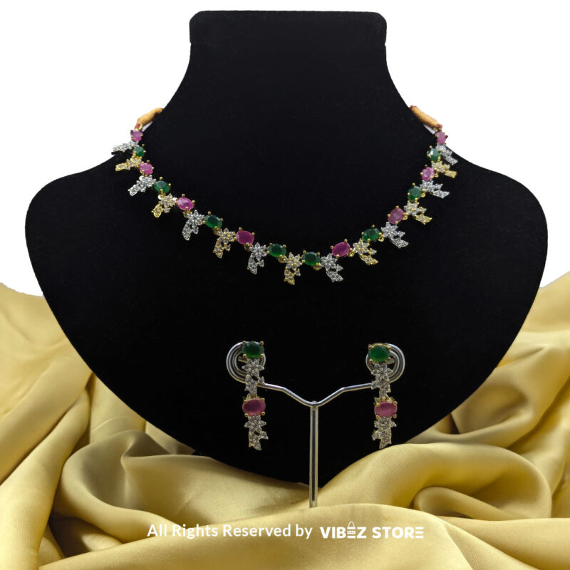 Multicolor gemstone necklace set with green and pink stones, paired with matching earrings, displayed on a black mannequin with a golden fabric backdrop.