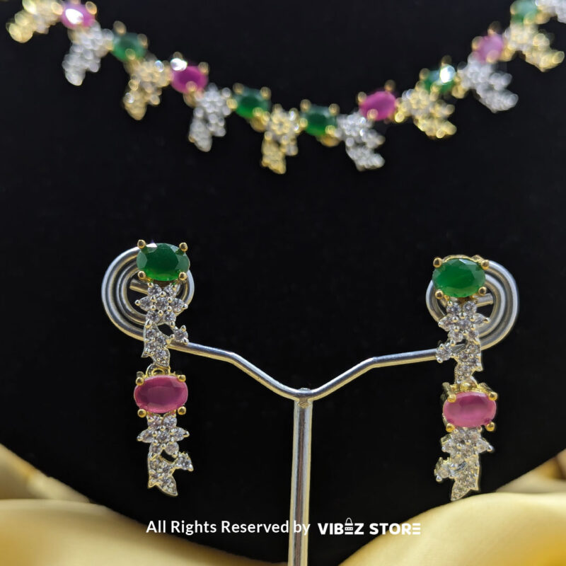 Multicolor gemstone necklace set with green and pink stones, paired with matching earrings, displayed on a black mannequin with a golden fabric backdrop.