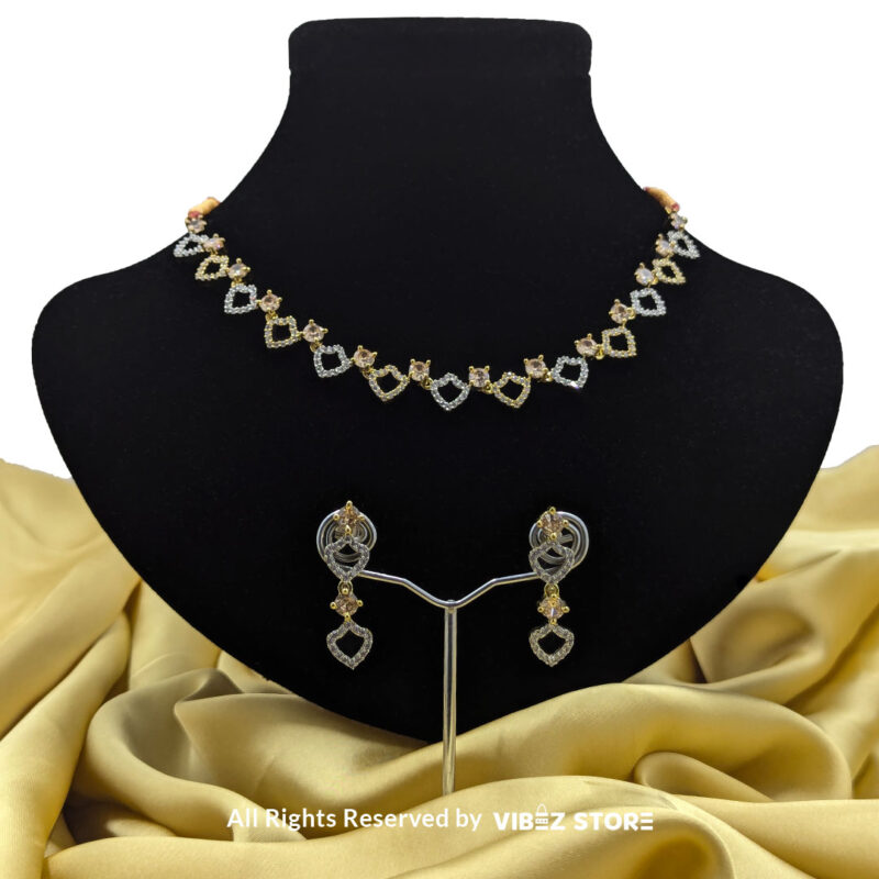 Heart-shaped necklace set with sparkling stones and matching earrings, displayed on a black mannequin with a golden fabric backdrop.