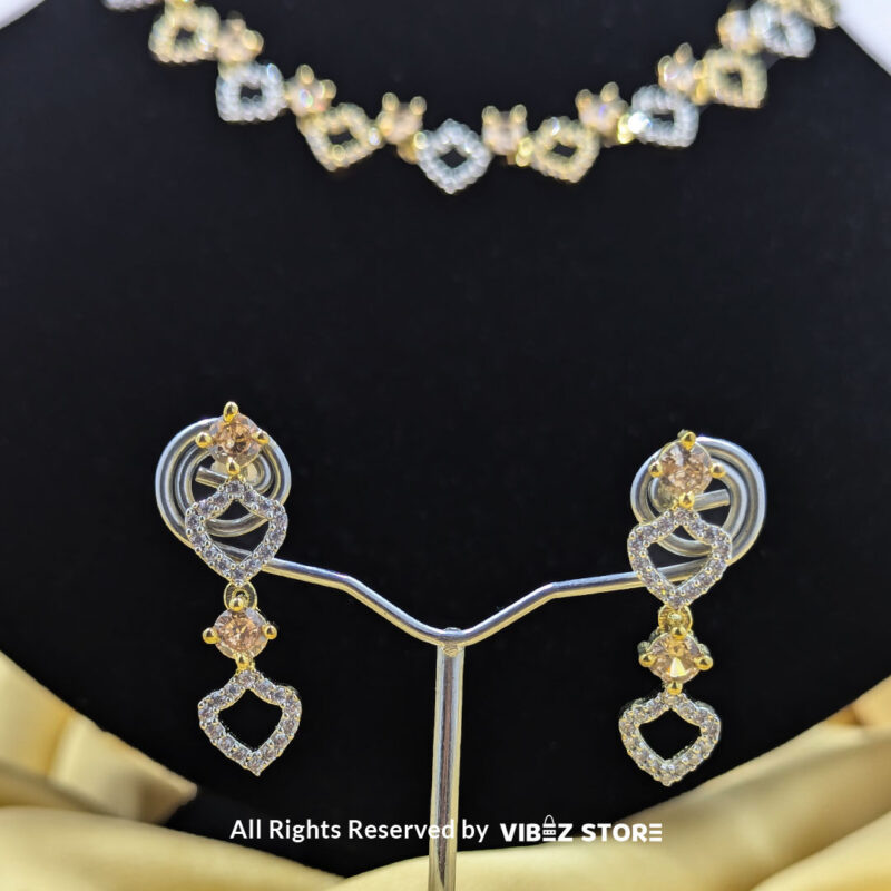 Heart-shaped necklace set with sparkling stones and matching earrings, displayed on a black mannequin with a golden fabric backdrop.