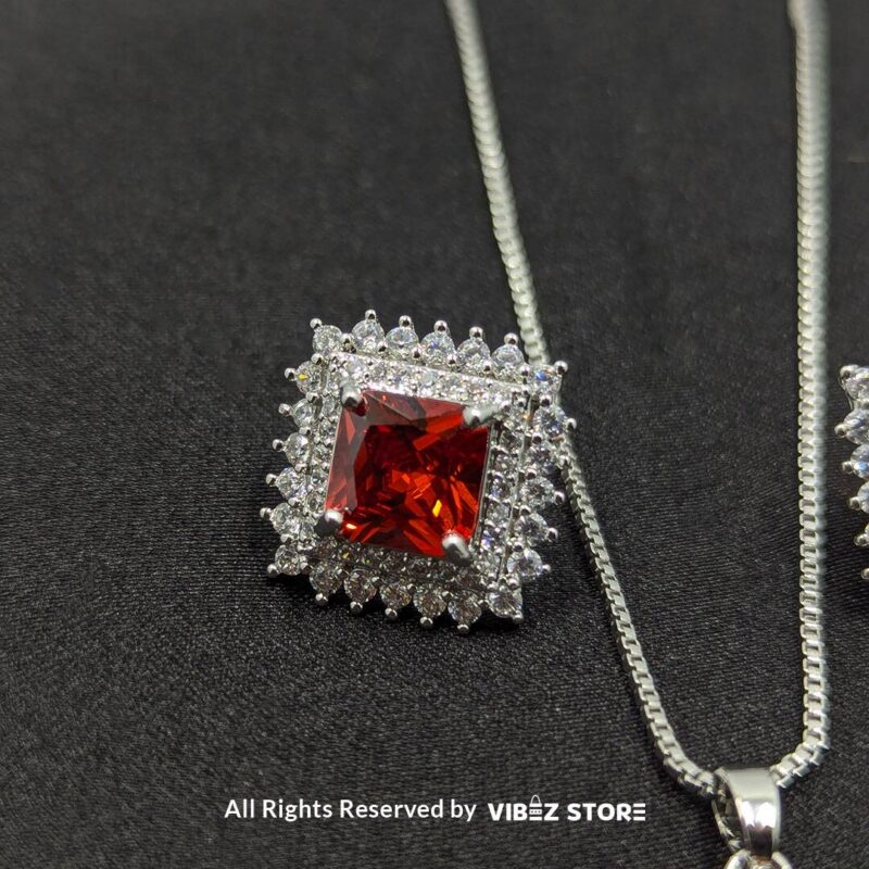 Ruby red square pendant jewelry set featuring a vibrant red gemstone necklace with matching stud earrings, surrounded by sparkling stones.