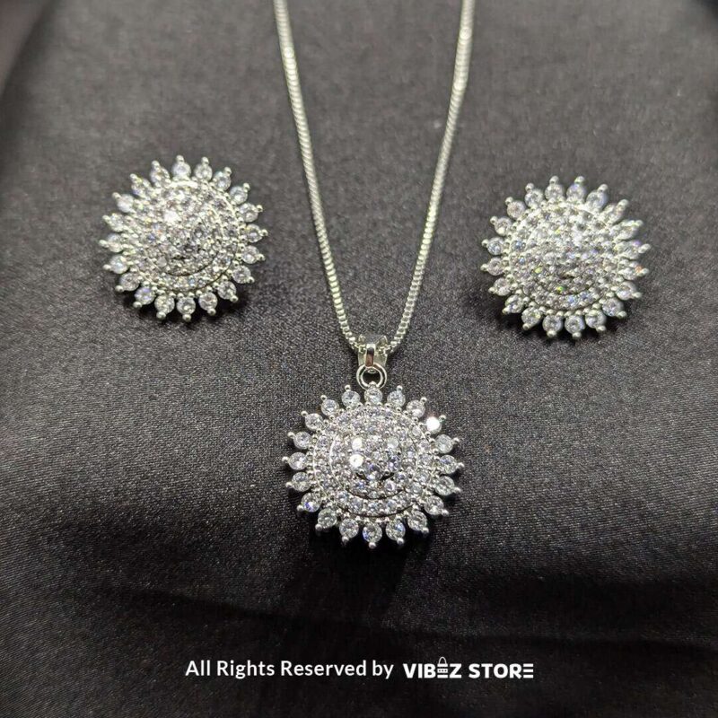 Starburst-shaped pendant and matching earrings adorned with shimmering crystals, displayed on a sleek black fabric.