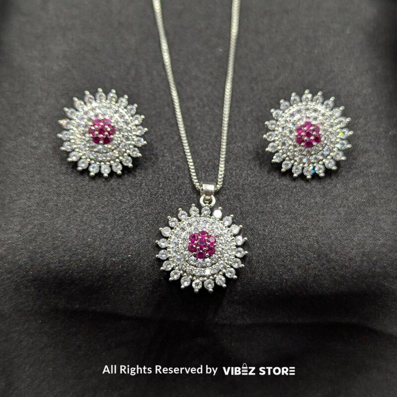 Ruby starburst pendant with matching earrings, featuring shimmering crystals and a vibrant ruby centerpiece, displayed on a sleek black fabric.