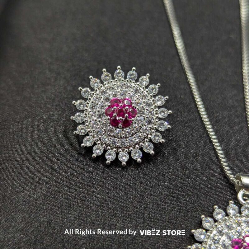 Ruby starburst pendant with matching earrings, featuring shimmering crystals and a vibrant ruby centerpiece, displayed on a sleek black fabric.