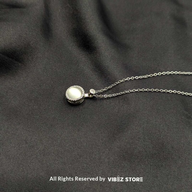 A silver rotating pearl locket pendant surrounded by sparkling accents, displayed on a black fabric background.