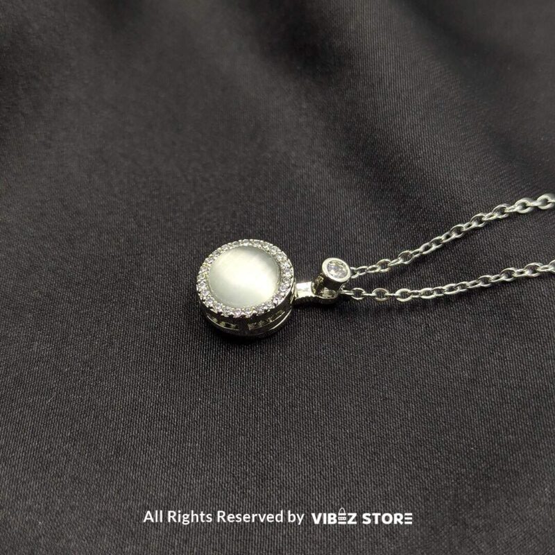 A silver rotating pearl locket pendant surrounded by sparkling accents, displayed on a black fabric background.