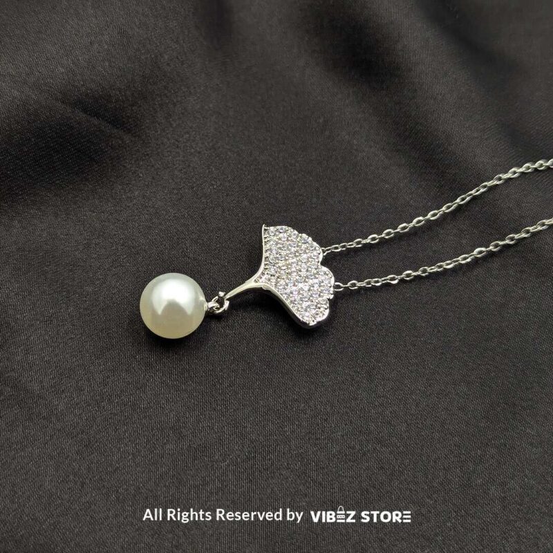 A silver locket featuring a sparkling leaf design with a pearl drop, perfect for adding elegance to any outfit.