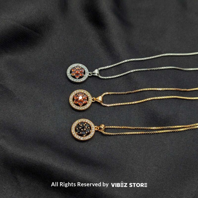 Three round lockets featuring floral gemstone designs (black, amber, and red) surrounded by crystal halos, displayed with gold-tone and silver-tone chains on a black fabric background.