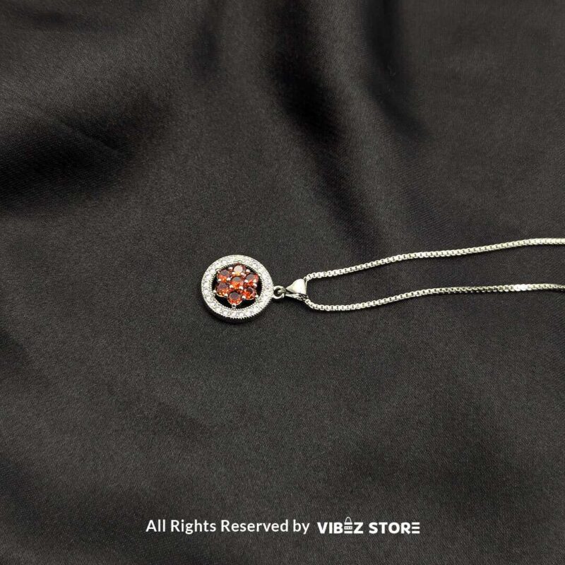 Three round lockets featuring floral gemstone designs (black, amber, and red) surrounded by crystal halos, displayed with gold-tone and silver-tone chains on a black fabric background.