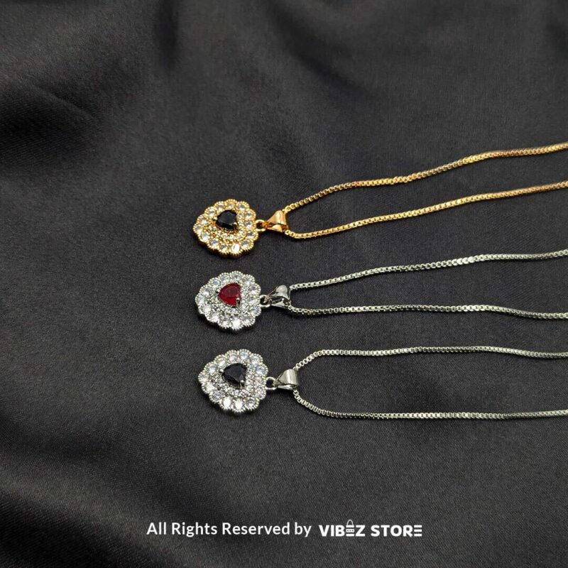 Three heart-shaped gemstone lockets in black and red, framed by dazzling crystals, displayed with gold-tone and silver-tone chains on a black fabric background.