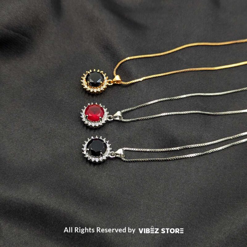 Three round gemstone lockets with crystal halos, displayed on gold-tone and silver-tone chains against a black fabric background.