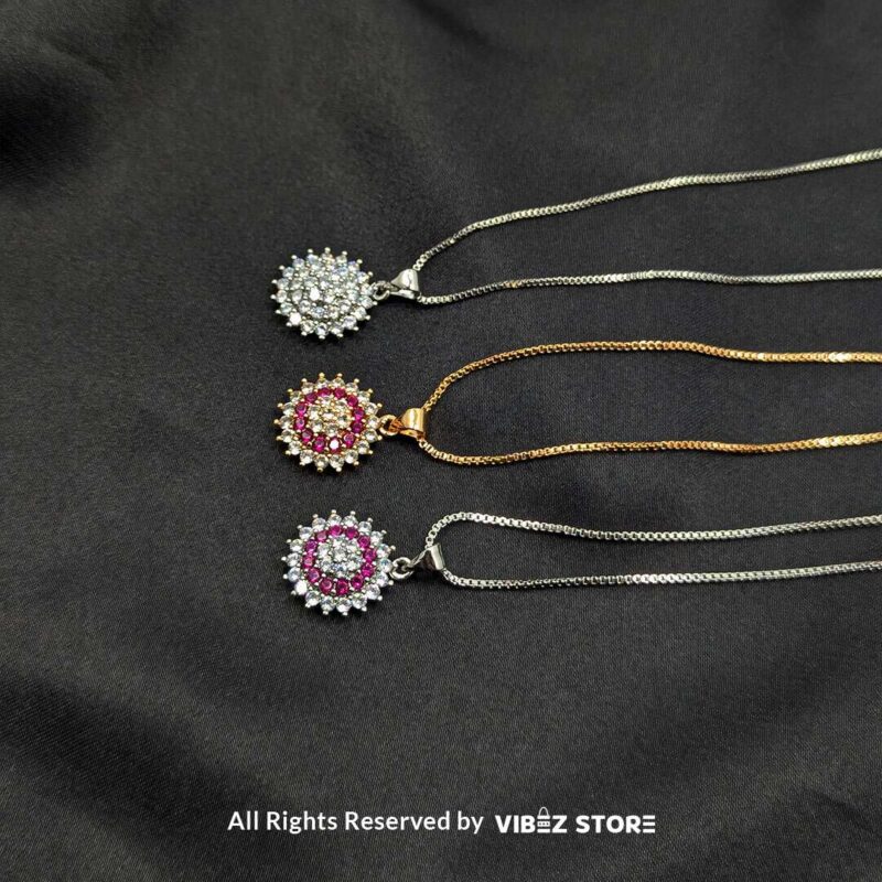 A collection of three gemstone lockets in clear, gold-pink, and silver-pink tones, each surrounded by a dazzling crystal halo, displayed on a black fabric background.