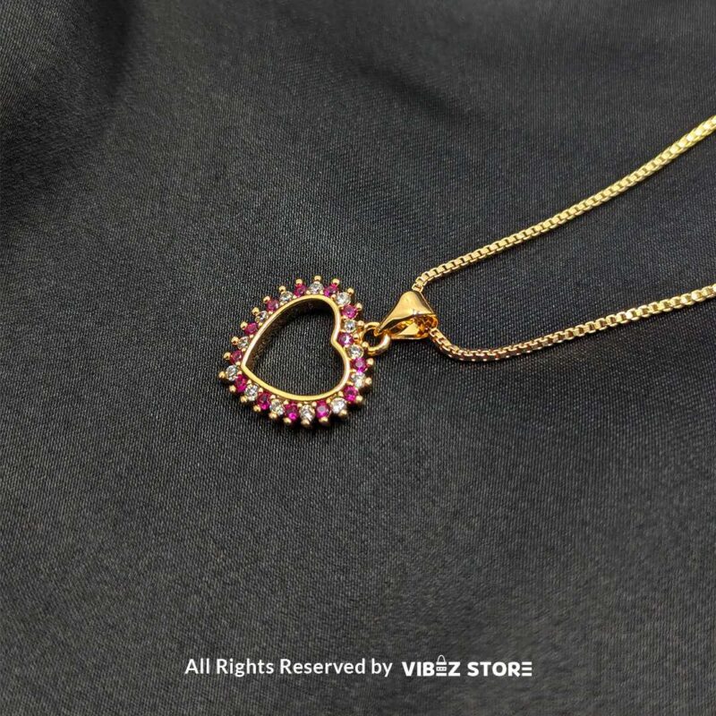 Gold heart-shaped open-frame locket with pink gemstone accents displayed on a black fabric background.