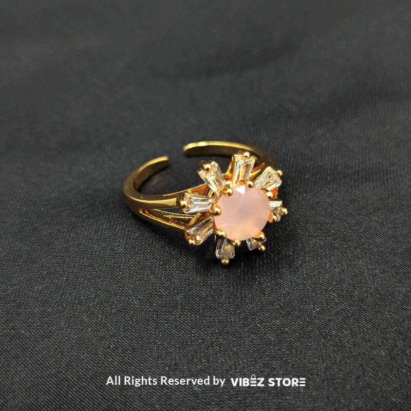 Gold-tone ring featuring a soft pink center stone with a halo of baguette crystals, a floral-inspired design from Vibez Store.